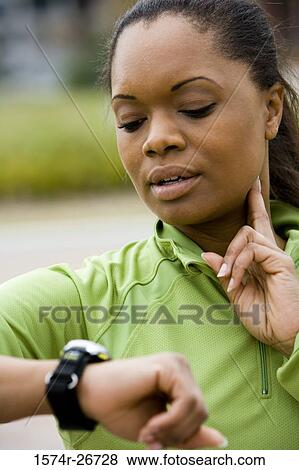 Stock Photo - Young woman in sports clothing looking her watch. Fotosearch