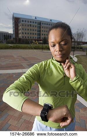 Young woman in sports clothing looking her watch with building in the background View Large Photo Image Stock Photograph - Young woman in sports clothing looking her watch with building in the background. Fotosearch