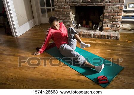 Stock Photo - Young woman in sports clothing exercising on mat by fire place. Fotosearch