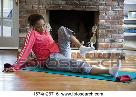 Stock Photograph - Young woman in sports clothing exercising on mat by fire place. Fotosearch