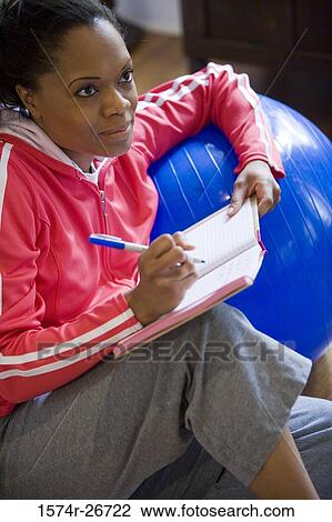 Young woman in sports clothing writing in a book by fitness ball View Large Photo Image Stock Image - Young woman in sports clothing writing in a book by fitness ball. Fotosearch