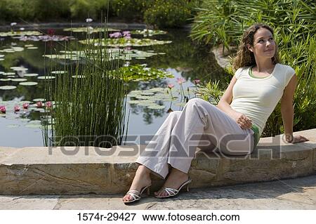 Stock Photo - Young woman sitting by pond. Fotosearch