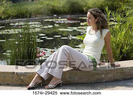 Young woman sitting by pond View Large Photo Image Stock Photography - Young woman sitting by pond. Fotosearch