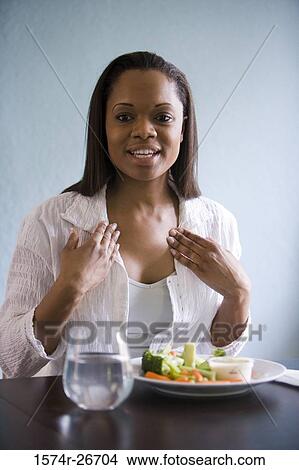 Young woman sitting by table with a plate of vegetables View Large Photo Image Picture - Young woman sitting by table with a plate of vegetables. Fotosearch