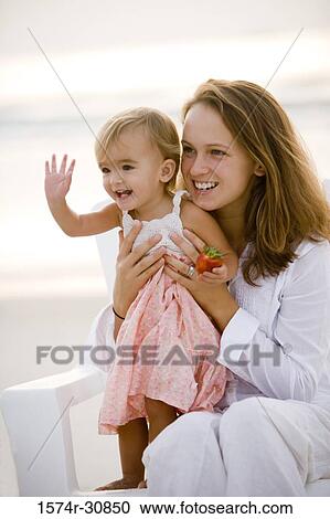 Young woman sitting with daughter waving hand View Large Photo Image Stock Image - Young woman sitting with daughter waving hand. Fotosearch