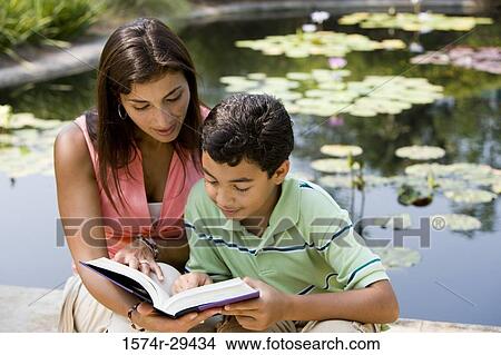 Young woman sitting with her son by pond reading book View Large Photo Image Picture - Young woman sitting with her son by pond reading book. Fotosearch