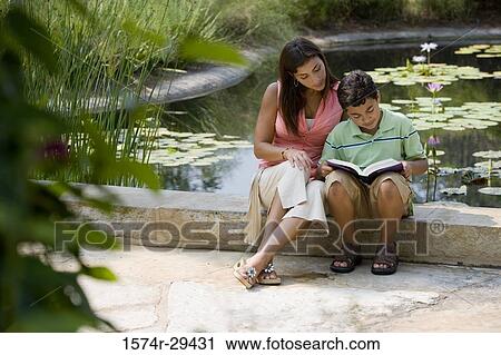 Young woman sitting with her son by pond reading book View Large Photo Image Stock Image - Young woman sitting with her son by pond reading book. Fotosearch