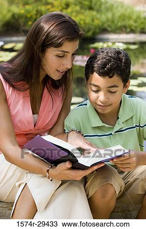 Young woman sitting with her son by pond reading book View Large Photo Image Stock Image - Young woman sitting with her son by pond reading book. Fotosearch