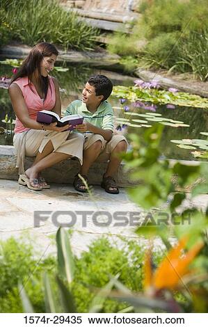 Young woman sitting with her son by pond reading book View Large Photo Image Stock Photography - Young woman sitting with her son by pond reading book. Fotosearch