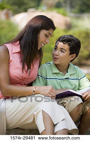 Stock Image - Young woman sitting with her son reading book. Fotosearch