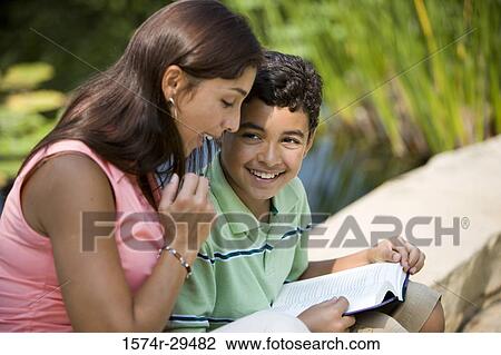 Stock Image - Young woman sitting with her son reading book. Fotosearch