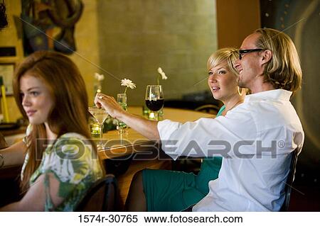 Stock Photography - Young woman with mature couple at table with drinks, smiling. Fotosearch