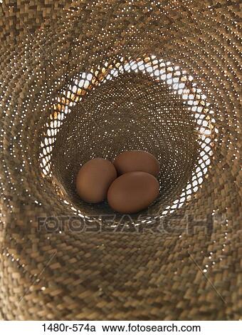 Stock Image - Brown eggs in a straw hat. Fotosearch