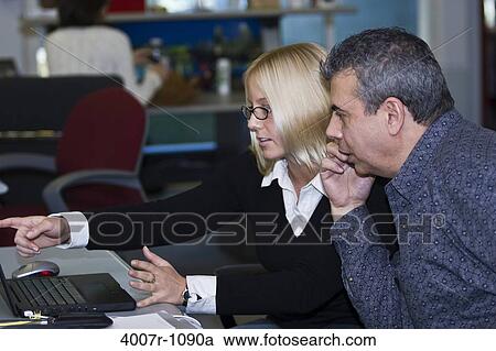 Stock Image - Business executives discussing in front of a laptop, Florida, USA. Fotosearch