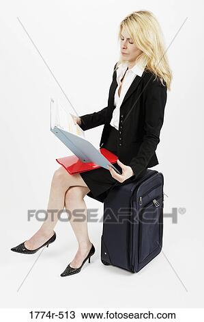 Stock Image - Businesswoman sitting on a luggage and reading files. Fotosearch