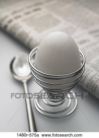 Stock Image - Close-up of a boiled egg in an eggcup with a newspaper. Fotosearch