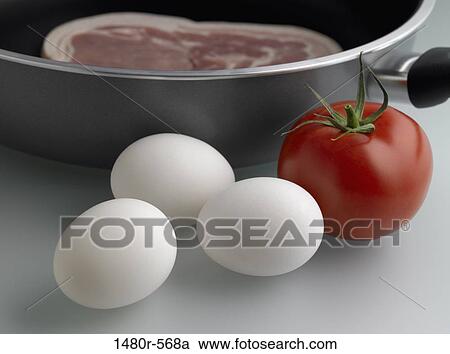 Stock Image - Close-up of a tomato with eggs and bacon in the pan. Fotosearch