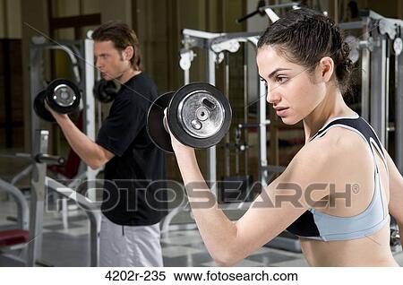 Close-up of a young woman exercising with dumbbells in a gym View Large Photo Image Stock Photography - Close-up of a young woman exercising with dumbbells in a gym. Fotosearch