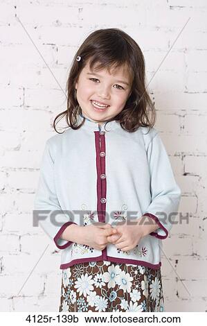 Stock Image - Mixed race Japanese girl smiling holding hands in studio with brick wall, USA. Fotosearch