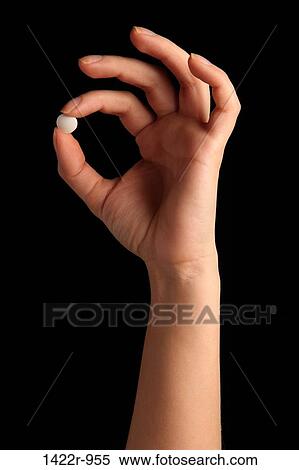 Stock Photography - Person's hand holding a white pill between the fingers. Fotosearch