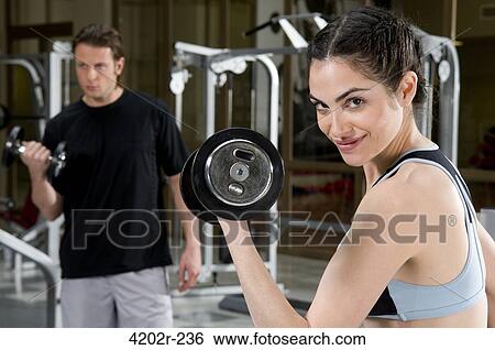 Portrait of a young woman exercising with dumbbells in a gym View Large Photo Image Stock Photograph - Portrait of a young woman exercising with dumbbells in a gym. Fotosearch