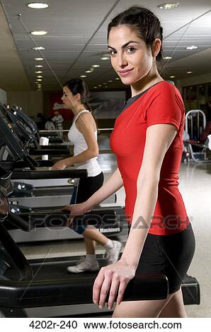 Stock Image - Two young women running on a treadmill in a gym. Fotosearch