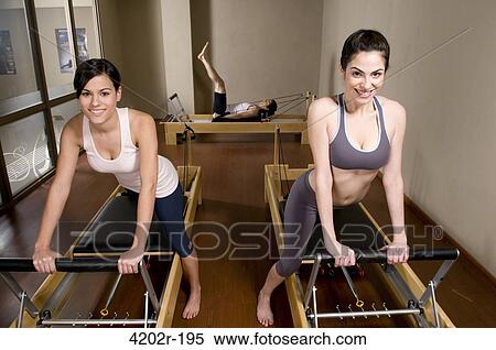 Two young women stretching up her legs with a Pilates's exercising machine at gym View Large Photo Image Stock Photography - Two young women stretching up her legs with a Pilates's exercising machine at gym. Fotosearch