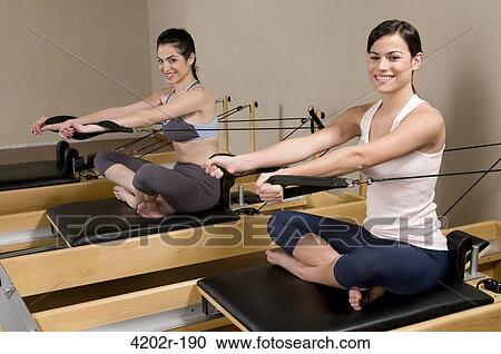 Two young women working out with Pilates exercise machine in a gym View Large Photo Image Stock Image - Two young women working out with Pilates exercise machine in a gym. Fotosearch