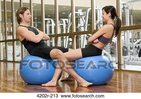 Stock Image - Young couple sitting on fitness balls in a gym. Fotosearch