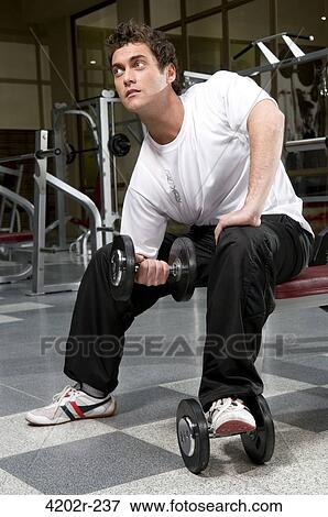 Stock Photo - Young man exercising with dumbbells in a gym. Fotosearch
