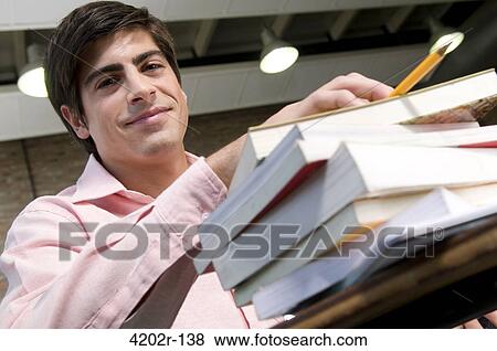 Young man in a classroom with pile of books View Large Photo Image Stock Photo - Young man in a classroom with pile of books. Fotosearch