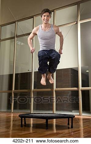 Young man jumping on a trampoline in a gym View Large Photo Image Stock Image - Young man jumping on a trampoline in a gym. Fotosearch