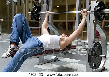 Young man lifting weights in a gym View Large Photo Image Stock Image - Young man lifting weights in a gym. Fotosearch
