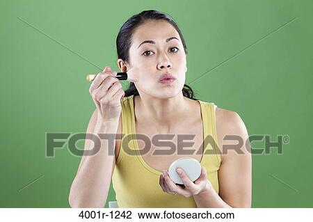 Stock Image - Young woman applying make-up on her face. Fotosearch