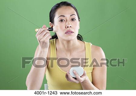 Stock Image - Young woman applying make-up on her face. Fotosearch