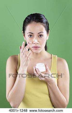 Stock Photo - Young woman applying moisturizer on her face. Fotosearch