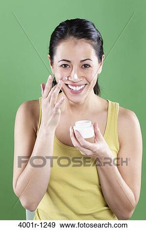 Stock Photo - Young woman applying moisturizer on her face. Fotosearch
