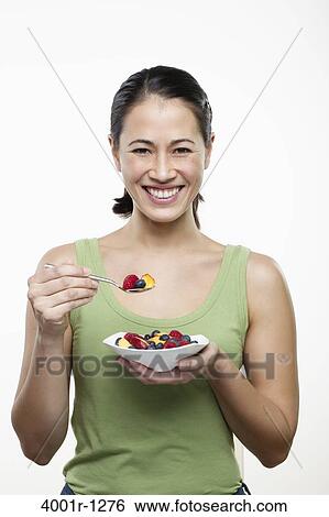 Stock Photograph - Young woman eating fruit salad and smiling. Fotosearch