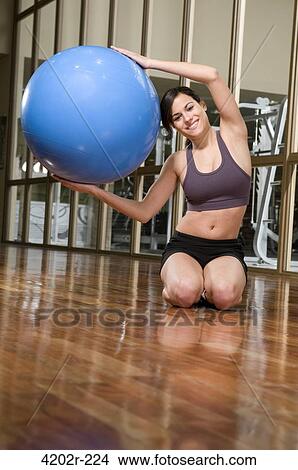 Young woman exercising with a fitness ball in a gym View Large Photo Image Picture - Young woman exercising with a fitness ball in a gym. Fotosearch