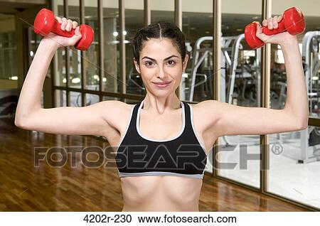 Young woman exercising with dumbbells in a gym View Large Photo Image Stock Image - Young woman exercising with dumbbells in a gym. Fotosearch