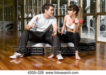 Young woman exercising with dumbbells with a young man sitting beside her View Large Photo Image Stock Photo - Young woman exercising with dumbbells with a young man sitting beside her. Fotosearch