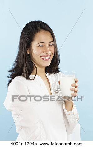Stock Image - Young woman holding a glass of milk and smiling. Fotosearch