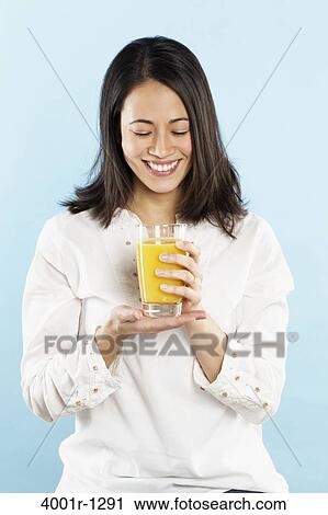 Stock Image - Young woman holding a glass of orange juice. Fotosearch