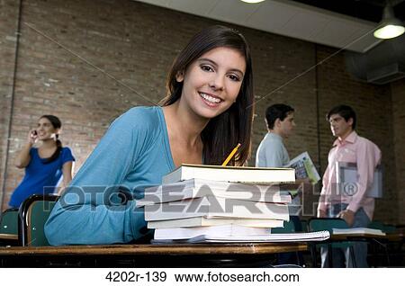 Stock Photo - Young woman in a classroom with pile of books. Fotosearch