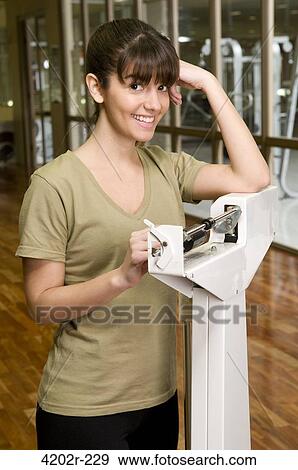 Stock Photo - Young woman weighing herself on scale. Fotosearch