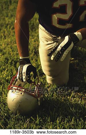 Stock Image - American football player kneeling on the field. Fotosearch