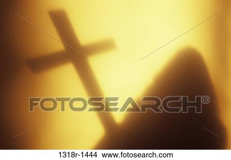 Atmospheric shadow or silhouette of hooded figure holding large crucifix in front of wall with glow of warm light Norfolk UK View Large Photo Image Picture - Atmospheric shadow or silhouette of hooded figure holding large crucifix in front of wall with glow of warm light Norfolk UK. Fotosearch