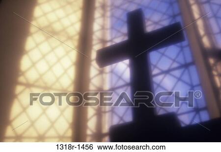 Stock Photograph - Atmospheric view of large wooden crucifix silhouetted against blue sky of leaded window with shadows Norfolk UK. Fotosearch