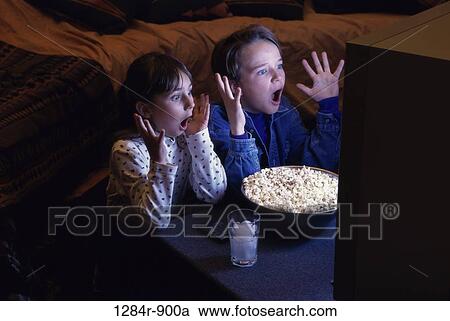 Boy and girl sitting in front of a bowl of popcorn watching television View Large Photo Image Stock Image - Boy and girl sitting in front of a bowl of popcorn watching television. Fotosearch