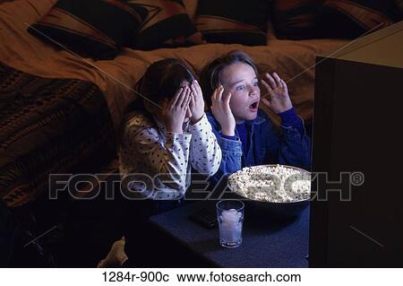 Stock Image - Boy and girl sitting in front of a bowl of popcorn watching television. Fotosearch